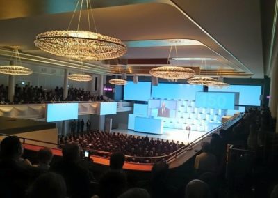 Festsaal, Politiker hält Rede auf der Bühne, Große Lampen hängen von der Decke