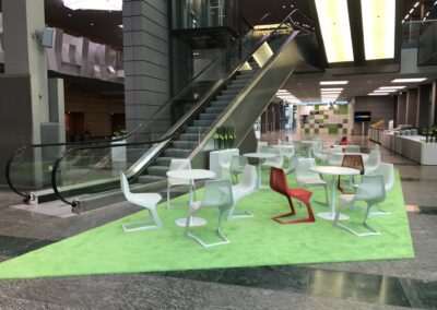 BASF Hauptversammlung, Foyer, Sitzecken mit weißen Tischen und weißen und roten Stühlen aus Metallgeflecht auf grünem Hochfloorteppich, Leuchtblumenkasten und Ausstellung