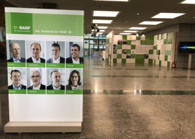 BASF Hauptversammlung, Foyer mit beleuchtetem Print Frame mit Plexi-Druck: Stele mit Vorstandsmitgliedern, im vorderen Bereich Ausstellung der BASF Themenwelten