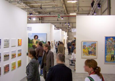 Blick durch einen Gang der Art Fair Messe in Köln, zu sehen sind mehrere Eingänge in die jeweiligen Ausstellungsräume, vereinzelt Exponate und mehrere Messebesucher
