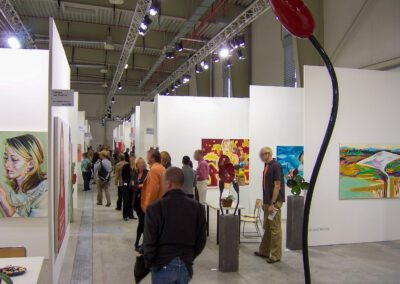 Blick durch einen Gang der Art Fair Messe in Köln, zu sehen sind mehrere Eingänge in die jeweiligen Ausstellungsräume, vereinzelt Exponate und mehrere Messebesucher