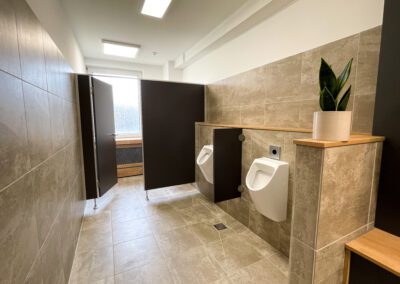 Herren-WC, Unterschrank Waschbecken mit schwarzen Fronten und Eicheholzplatte, Wand- und Bodenfliesen in Betonoptik, Urinale und WC Kabine, Zimmerpflanze