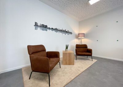 Besprechungsraum, Folienschnitt mit Duisburger Skyline, Hängelampe, Sitzecke mit braunen Sesseln und Coffeetable auf beigem Teppich, graue Stehlampe