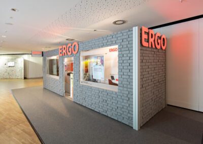 Begehbarer ERGO Messestand mit grauer Backsteinwand und grauem Teppichboden, Fernerkennung, Schaufenster mit Werbetafeln