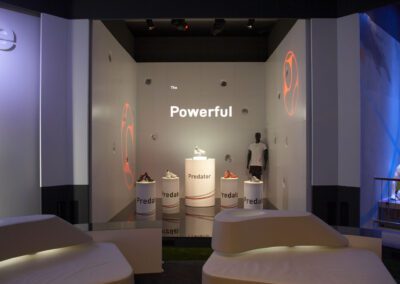 Showroom mit teils beleuchteten Säulen, auf dem adidas Schuhe ausgestellt werden und einer Schaufensterpuppe, Gobos zur Beleuchtung der Wände, weiße, beleuchtete Kunstleder Lounges