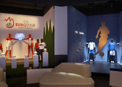 adidas Ausstellung im Showroom, zwei Stände: einer mit Säulen für Fußbälle und dahinter Schaufensterpuppen, daneben ein dunkler Stand im Storedesign