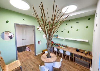 Kinderspielbereich der Arztpraxis mit einem Baum in der Raummitte und Spielzeug im Raum