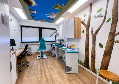 Untersuchungsraum für Kinder mit Deckenmotiv mit Stofftieren und Wandgestaltung mit Bäumen